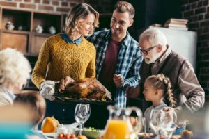 family around dinner table and lady holding turkey on platter