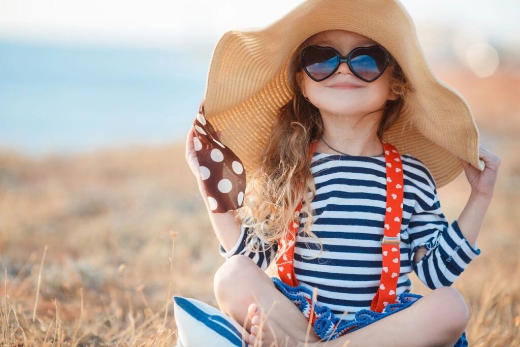 girl wearing beach hat and heart shaped lens sunglasses sitting on beach