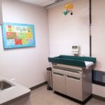 Exam room with pediatric exam table. white walls. gray floor.